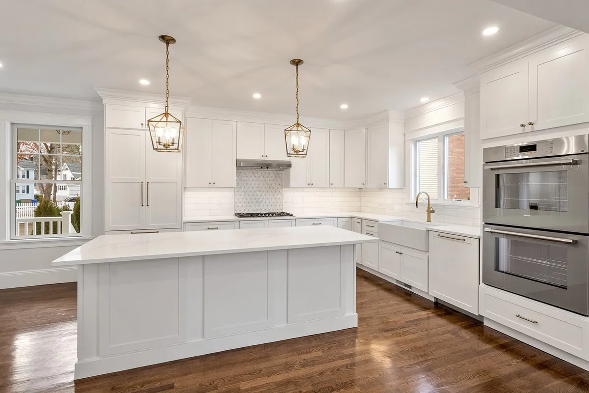 Newton kitchen with white shaker cabinets, a marble island, brass lantern pendants, and stainless wall ovens
