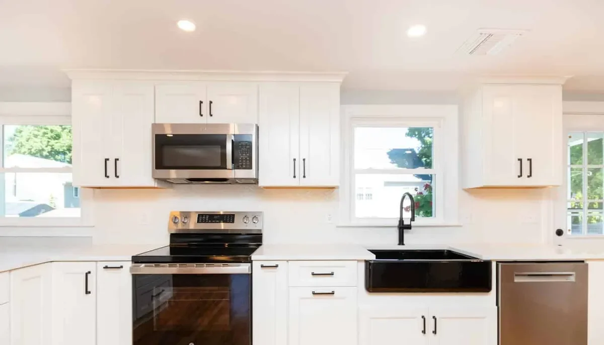Waltham kitchen range wall with white cabinets, a black cooktop, stainless hood, and a black farmhouse sink