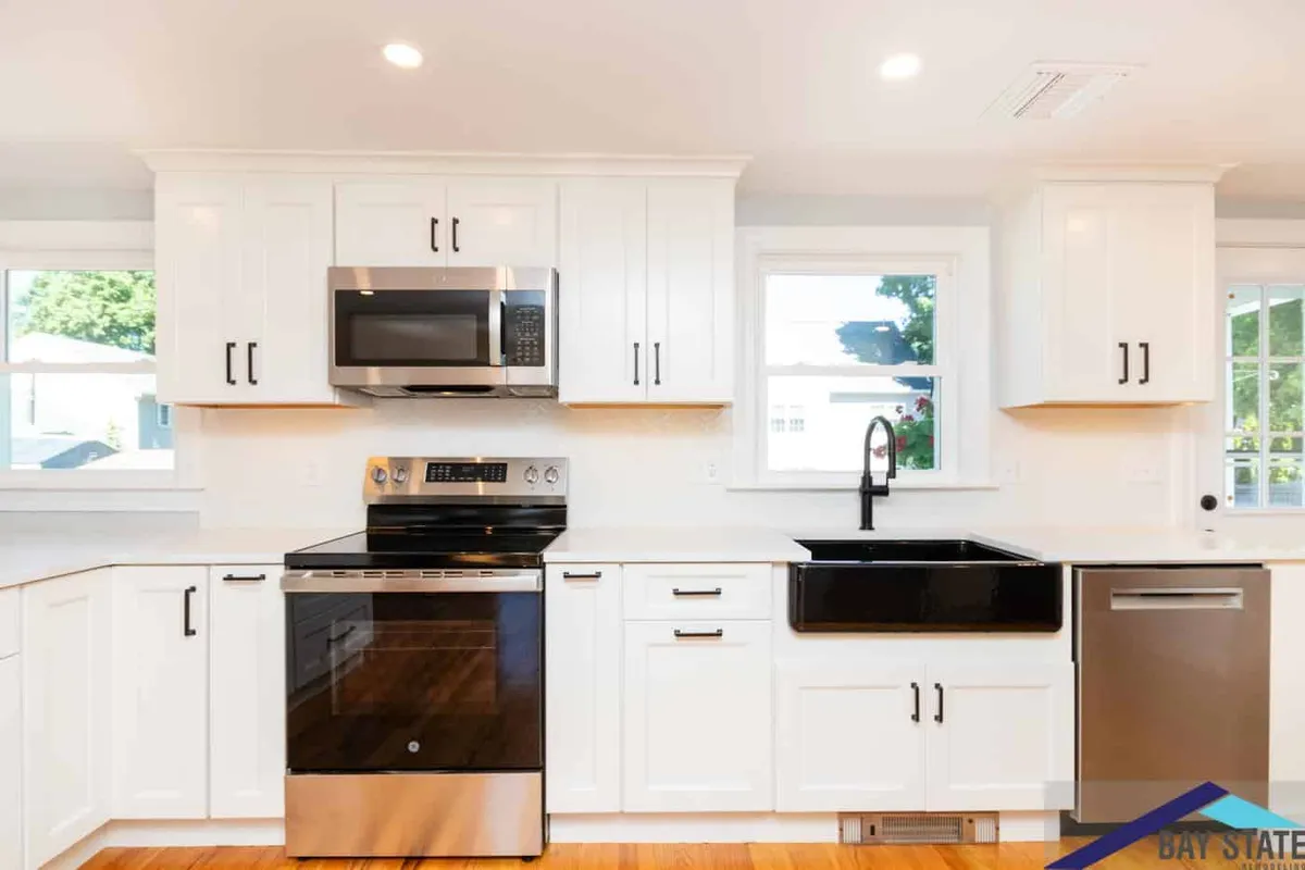 Waltham kitchen range wall with white cabinets, a black cooktop, stainless hood, and a black farmhouse sink