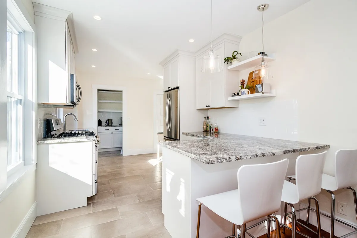 Arlington galley kitchen with white cabinets, a granite peninsula, stainless fridge, and glass pendant lighting