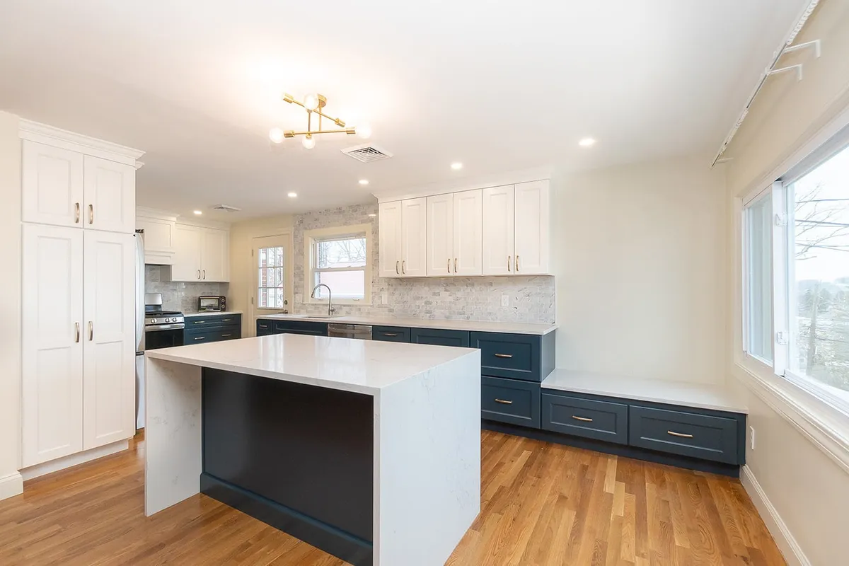 Roslindale kitchen with white upper cabinets, navy lower cabinets, and a quartz waterfall island