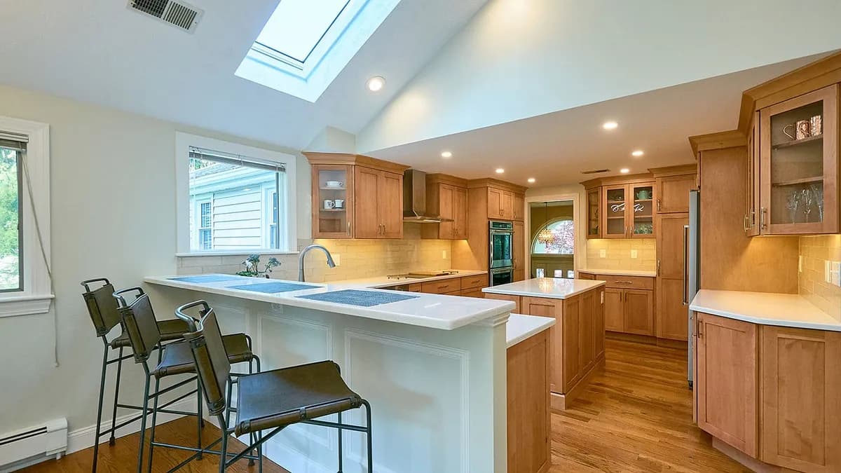 Wellesley kitchen with honey oak cabinets, a white peninsula counter, and a skylight over the island