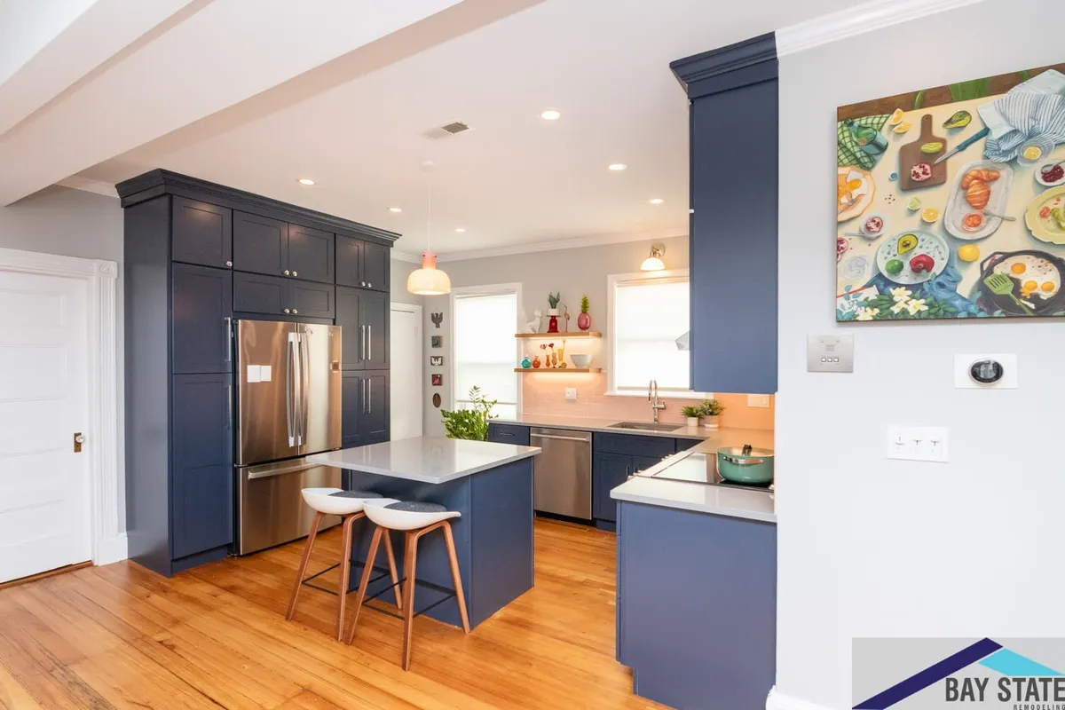 Wide view of the navy Jamaica Plain kitchen with island seating, stainless fridge wall, and pink tile backsplash