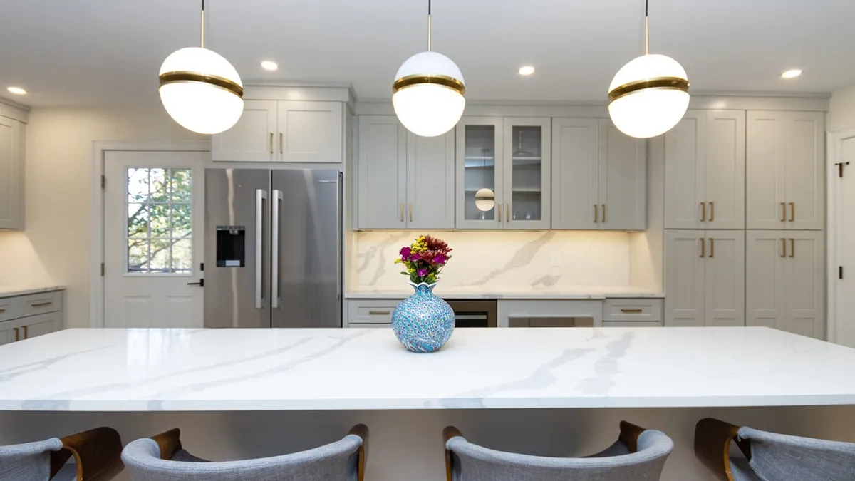 Jamaica Plain kitchen with light gray shaker cabinets, brass globe pendants, and a quartz waterfall island