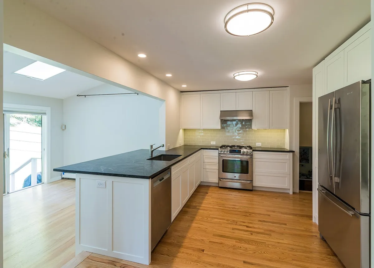 Newton kitchen with white shaker cabinets, black soapstone counters, green subway tile backsplash, and stainless appliances