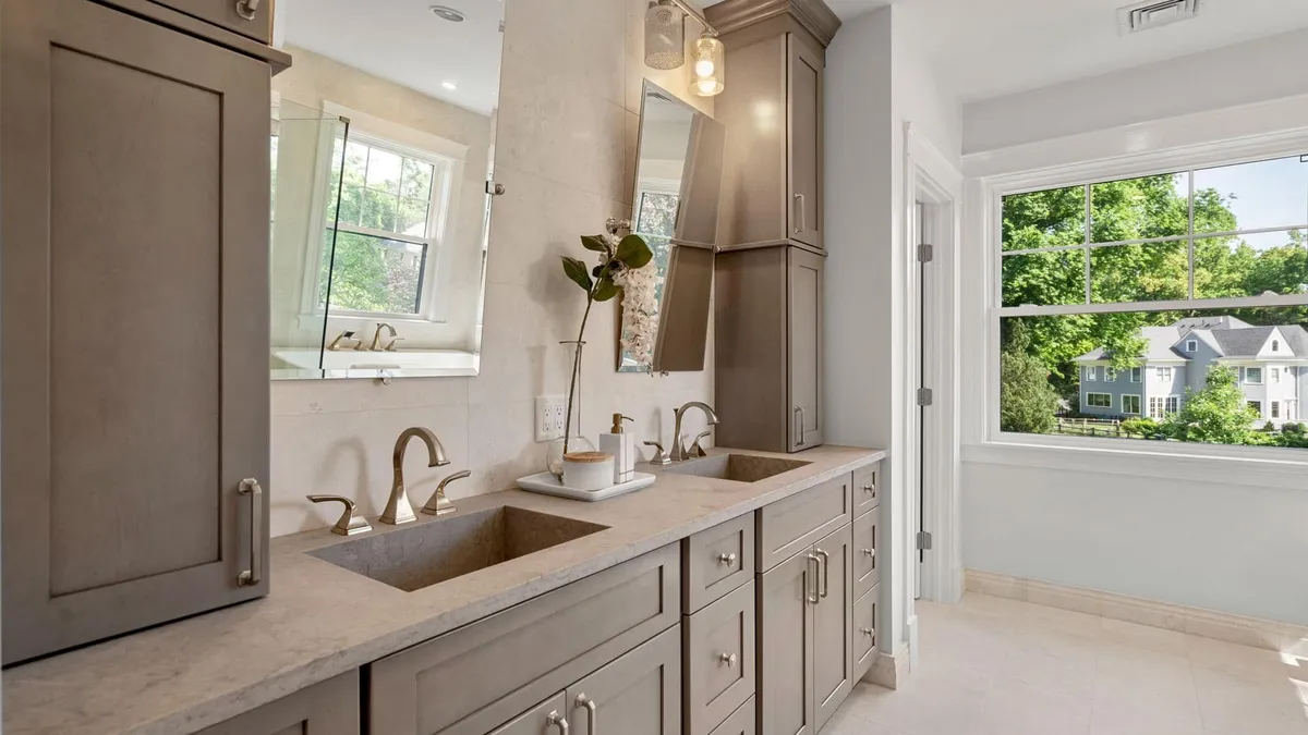 Newton primary bathroom with a double vanity, stone-look counter, and a picture window overlooking the yard