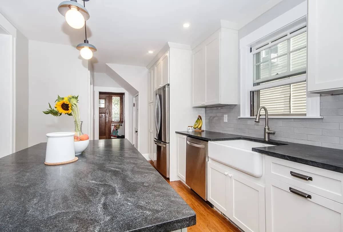 Roslindale kitchen with white farmhouse sink, dark stone waterfall island, and gray subway tile backsplash