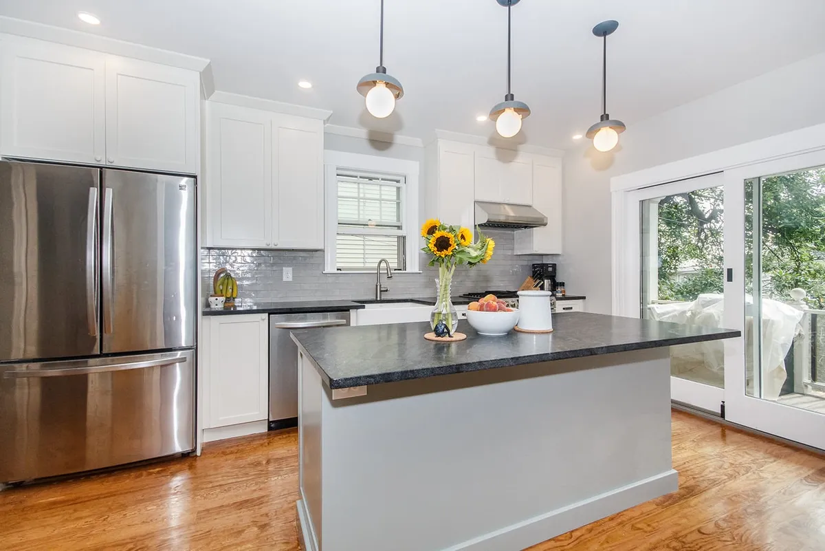 Roslindale kitchen with a dark stone waterfall island, white cabinets, stainless fridge, and gray subway tile