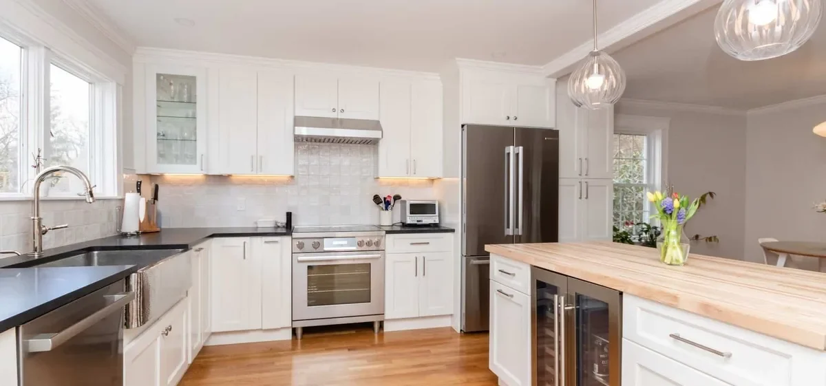 Renovated Newton kitchen with a butcher-block island, built-in wine fridge, glass globe pendants, and stainless appliances