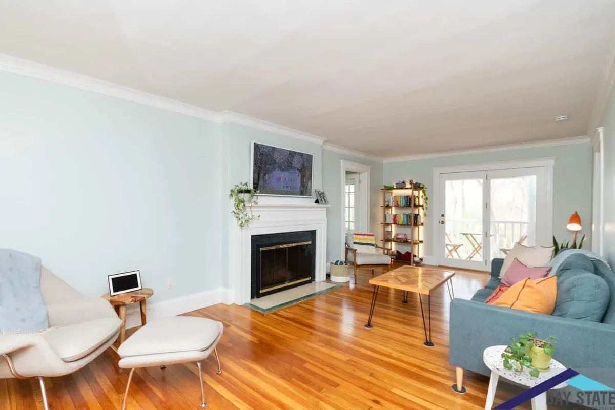 Adjoining Newton living room with a wood-mantel fireplace, hardwood floors, and French doors to the deck