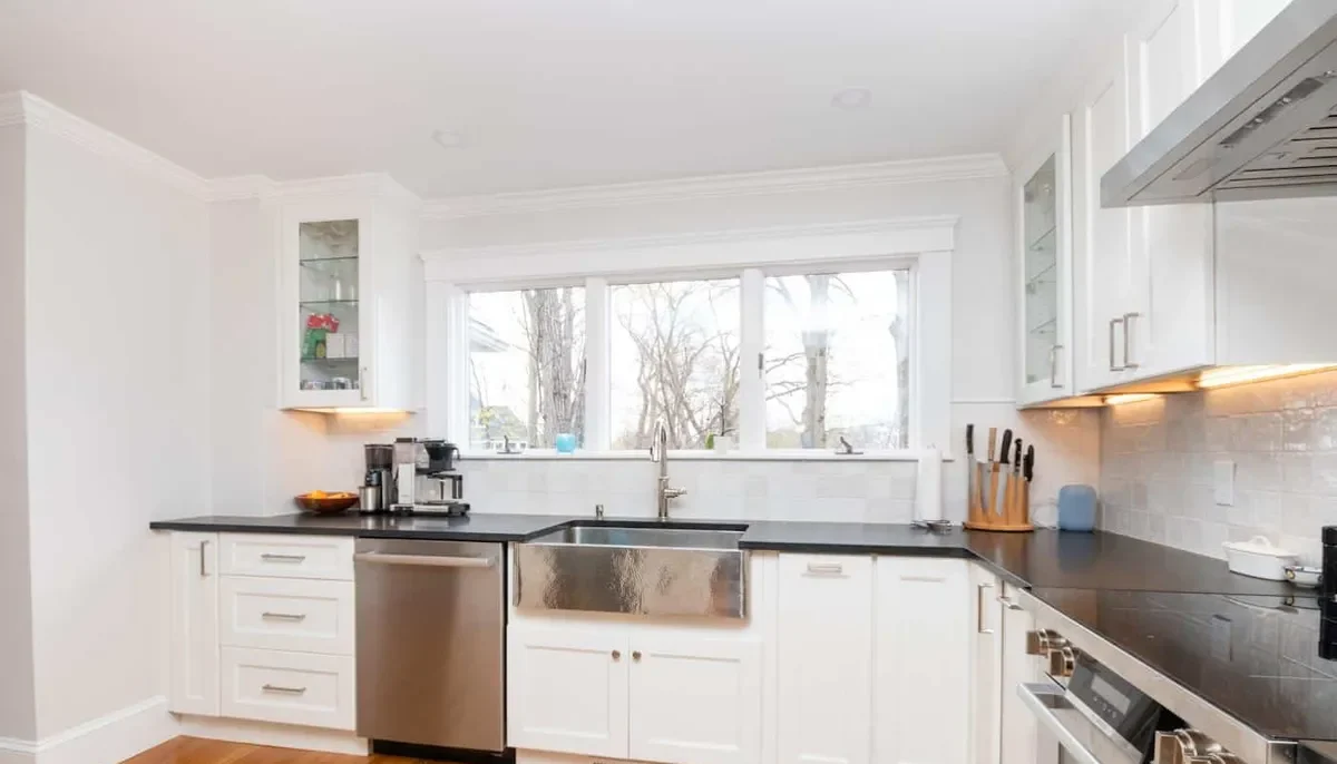 Newton kitchen with white shaker cabinets, black countertops, subway tile backsplash, and a stainless farmhouse sink