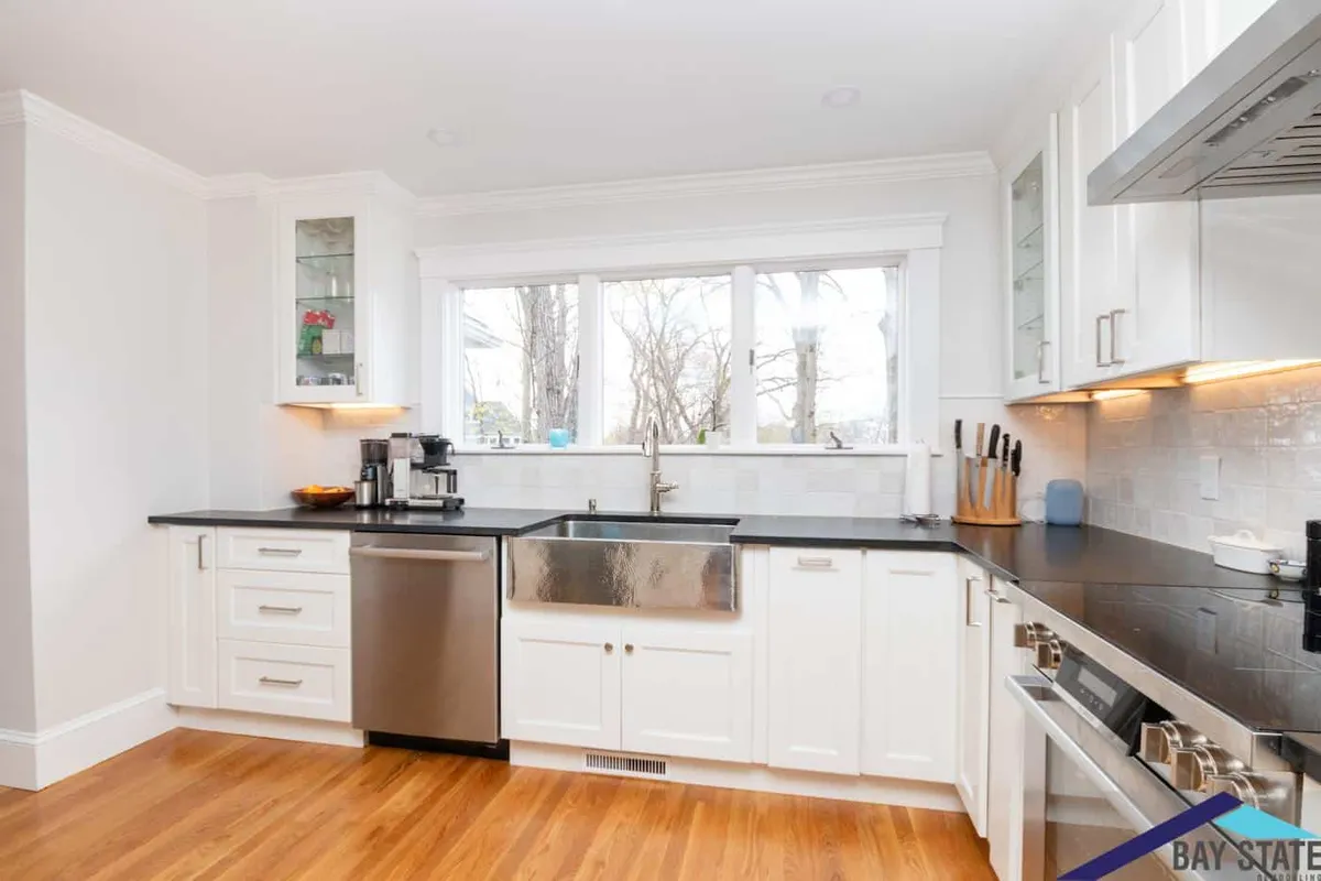 Newton kitchen with white shaker cabinets, black countertops, subway tile backsplash, and a stainless farmhouse sink