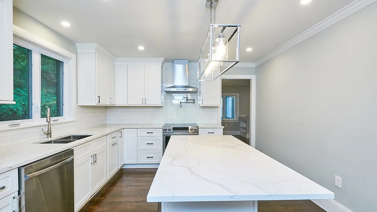 Newton kitchen with white shaker cabinets, a marble waterfall island, and chrome pendant lighting
