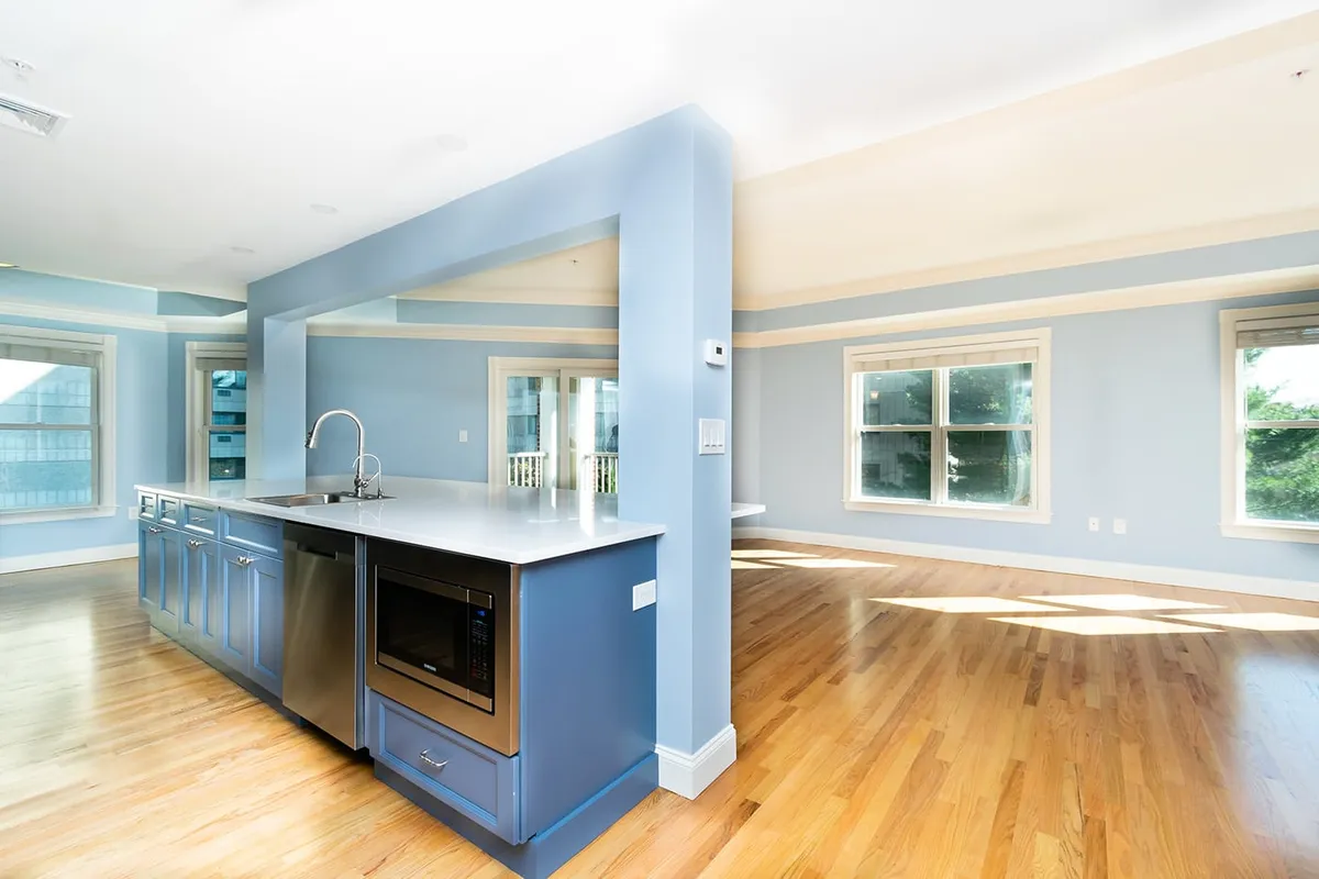 Brookline kitchen island with built-in microwave, blue cabinetry, opening to an empty sunlit living room