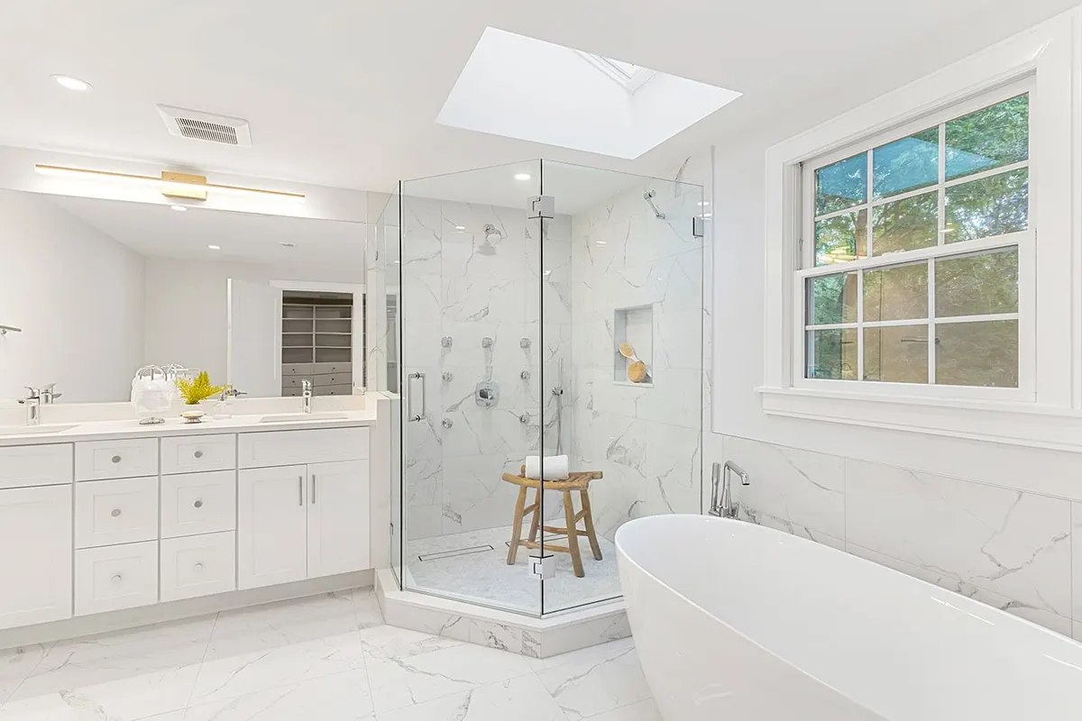 Bathroom with glass-enclosed shower, skylight, freestanding tub, and white vanity in the background