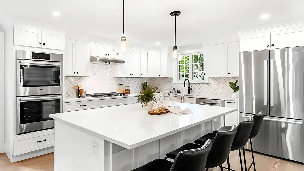 White quartz island countertop in a kitchen with white shaker cabinets, herringbone backsplash, and stainless appliances