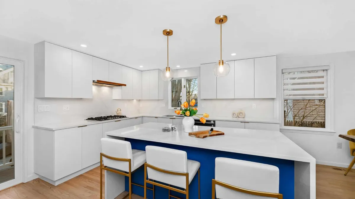 White quartz waterfall-edge island countertop over a blue base, with white cabinets and gold pendant lights